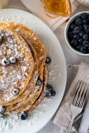 Tasty breakfast of pancakes with blueberries, powdered sugar, milk and honey
